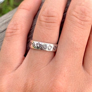 May include: A silver ring with a repeating pattern of cacti and geometric shapes.
