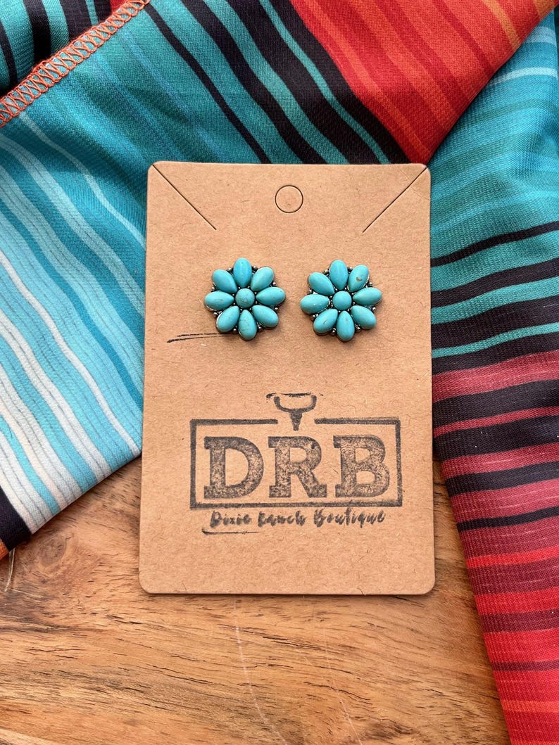 May include: Turquoise flower stud earrings on a brown card with the DRB Dixie Ranch Boutique logo. The earrings are set against a colourful striped fabric background.