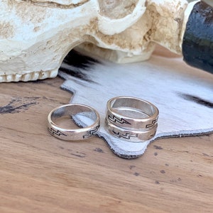 May include: Two silver rings with a lightning bolt design. The rings are stacked on top of each other and are sitting on a white surface.