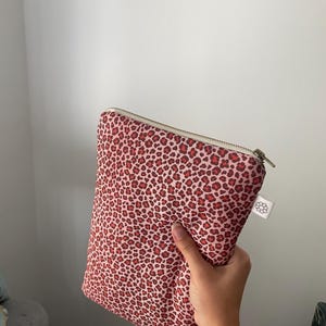 Può includere: Una pochette rosa e rossa con stampa leopardata e chiusura a zip. La pochette rettangolare ha una piccola etichetta bianca attaccata. La cerniera è color argento.