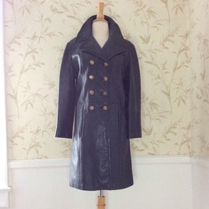 May include: A long black leather coat with a double breasted closure and gold buttons. The coat is on a wooden mannequin.