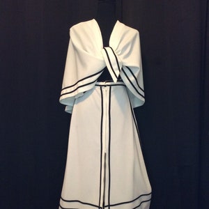 May include: A white dress with black trim and embroidered flowers. The dress has a long skirt and a cape-like top.