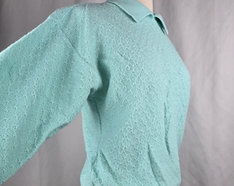 May include: A light turquoise knit polo shirt with a collared neckline and long sleeves. The shirt has a textured pattern and a ribbed hem and cuffs. The garment is displayed on a mannequin.
