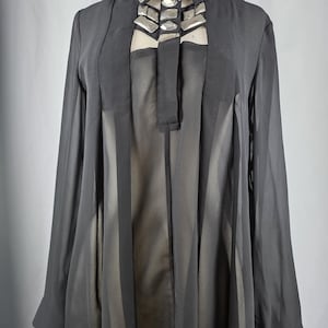 May include: Black long-sleeve blouse with a sheer, pleated front. The blouse features a high collar adorned with silver-toned geometric embellishments. The sleeves are long and the fabric appears lightweight.