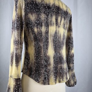 May include: A long-sleeved blouse with a unique pattern in shades of brown, tan, and white. The blouse features a high collar and flared sleeves. The fabric has a speckled design, creating a textured appearance. The garment is displayed on a mannequin.