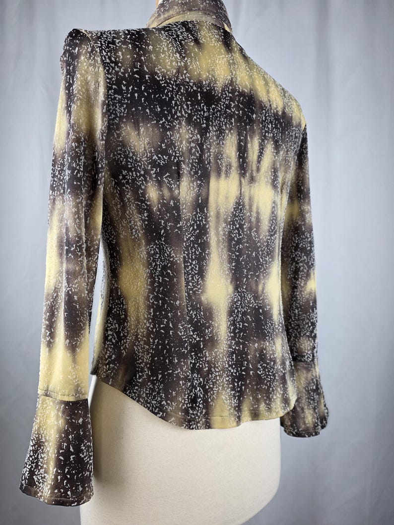 May include: A long-sleeved blouse with a unique pattern in shades of brown, tan, and white. The blouse features a high collar and flared sleeves. The fabric has a speckled design, creating a textured appearance. The garment is displayed on a mannequin.