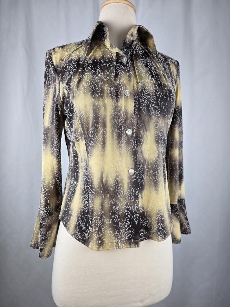 May include: A button-down shirt with a unique pattern of yellow, brown, and white. The long-sleeved shirt has a collared neckline and is displayed on a mannequin. The fabric has a textured appearance.