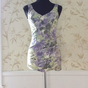 May include: A sleeveless dress with a floral print in shades of purple, green, and white. The dress has a V-neckline and a fitted silhouette.