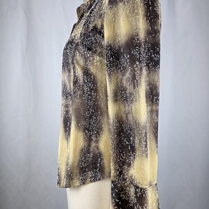 May include: A long-sleeved blouse with a unique pattern. The blouse features a mix of brown, tan, and white speckles. The fabric has a semi-sheer quality, and the sleeves have a slight flare at the wrist. The blouse is buttoned up the front.
