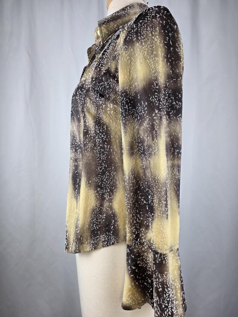May include: A long-sleeved blouse with a unique pattern. The blouse features a mix of brown, tan, and white speckles. The fabric has a semi-sheer quality, and the sleeves have a slight flare at the wrist. The blouse is buttoned up the front.