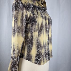 May include: A long-sleeved button-down shirt with a unique pattern. The shirt features a blend of brown, tan, and white colors, creating a textured, abstract design. The collar and cuffs are visible, and the shirt appears to be made of a lightweight fabric.