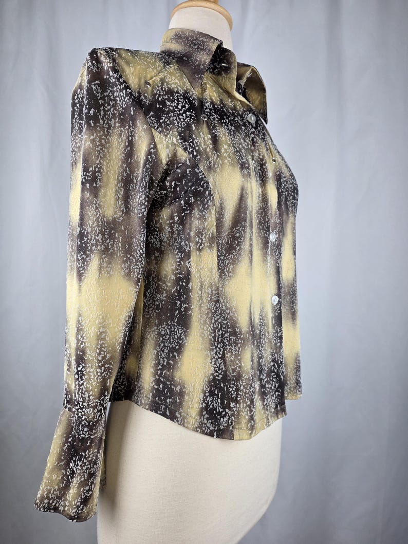 May include: A long-sleeved button-down shirt with a unique pattern. The shirt features a blend of brown, tan, and white colors, creating a textured, abstract design. The collar and cuffs are visible, and the shirt appears to be made of a lightweight fabric.