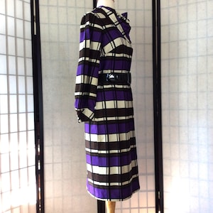 May include: A purple, white, and brown plaid dress with a black belt. The dress has long sleeves and a collared neckline.