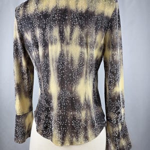May include: A long-sleeved blouse with a unique pattern. The blouse features a collared neckline and flared sleeves. The fabric has a mottled design in shades of brown, tan, and white, creating a textured appearance. The blouse is displayed on a mannequin.
