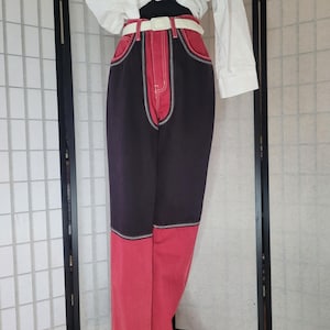 May include: Black and red denim pants with white stitching and a white belt. The pants have a unique design with the top half being black and the bottom half being red.