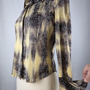 May include: A long-sleeved button-down shirt with a unique pattern. The shirt features a blend of yellow, brown, and white colors, creating a textured, abstract design. The collar and cuffs are visible, and the shirt is displayed on a mannequin.