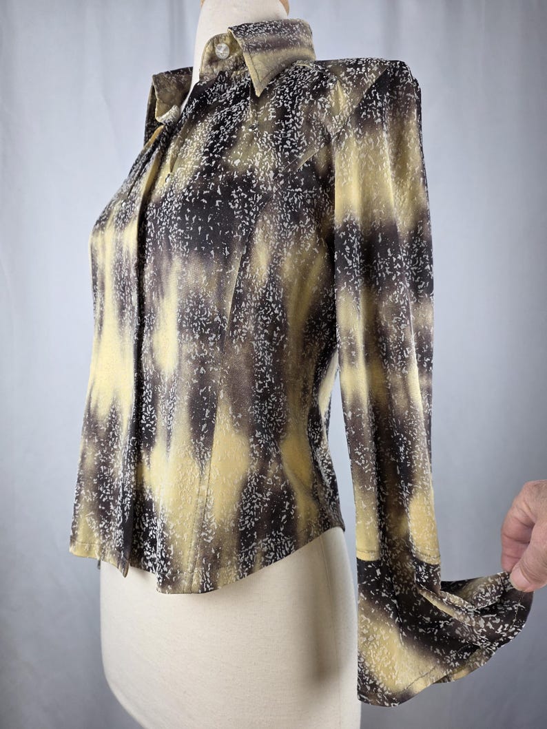 May include: A long-sleeved button-down shirt with a unique pattern. The shirt features a blend of yellow, brown, and white colors, creating a textured, abstract design. The collar and cuffs are visible, and the shirt is displayed on a mannequin.