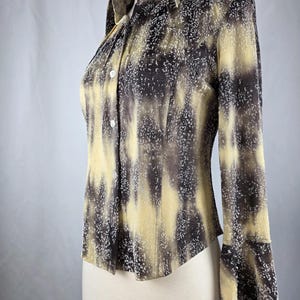 May include: A long-sleeve button-down shirt with a unique pattern. The shirt features a blend of brown and yellow hues with a speckled design. The collar and cuffs are visible, and the shirt is displayed on a mannequin.