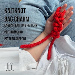 Könnte beinhalten: Ein leuchtend roter Strick-Taschenanhänger. Der Anhänger hat ein geknotetes Design mit einem langen, geflochtenen Schwanz. Das Bild enthält auch den Text "KNITKNOT BAG CHARM", "ENGLISH KNITTING PATTERN", "PDF DOWNLOAD" und "PATTERN SUPPORT".
