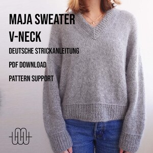 Könnte beinhalten: Ein grauer Strickpullover mit V-Ausschnitt und langen Ärmeln. Der Pullover wird an einem Model gezeigt, das eine blaue Jeans trägt. Der Text "MAJA SWEATER V-NECK" wird über dem Model angezeigt. Der Text "DEUTSCHE STRICKANLEITUNG" wird unter dem Model angezeigt. Der Text "PDF DOWNLOAD" wird unter dem Text "DEUTSCHE STRICKANLEITUNG" angezeigt. Der Text "PATTERN SUPPORT" wird unter dem Text "PDF DOWNLOAD" angezeigt.