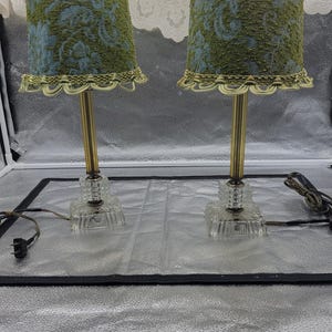 May include: A pair of vintage table lamps with green and blue patterned lampshades and gold metal bases. The bases are made of clear glass with a faceted design.
