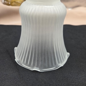 May include: A frosted glass lampshade with a fluted design. The lampshade has a flared shape and a scalloped edge. The glass is opaque and appears to be made of a thick material. The lampshade is designed to diffuse light.