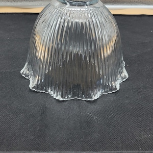 May include: A clear glass lampshade with a fluted design. The shade has a scalloped edge and a smooth, rounded top.