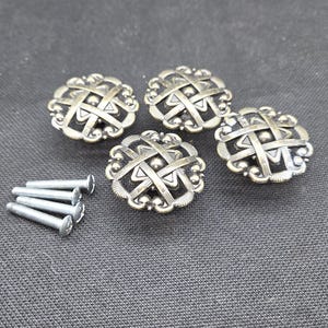 May include: Four antique brass cabinet knobs with a woven design, along with four silver screws. The knobs have a detailed, ornate pattern and are likely for furniture restoration or DIY projects.