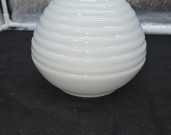 May include: A white, opaque, round vase with a ribbed, horizontal design. The vase has a small, cylindrical neck and a smooth, glossy finish. The vase is sitting on a black surface.