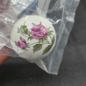 May include: White ceramic knob with a pink rose and green leaves design.