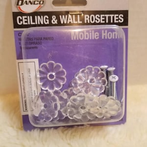 May include: Clear, flower-shaped ceiling and wall rosettes with mounting screws, packaged in a clear plastic container. The package has the text "CEILING & WALL ROSETTES" and the Danco logo.