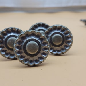 May include: Five antique-style metal drawer pulls with a circular design and a raised, scalloped edge. The pulls are a dark, aged bronze color.