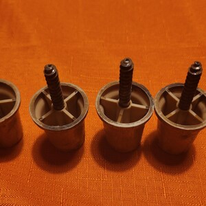 May include: Four brown plastic furniture leg caps with black screws. Each cap has five holes for attaching to furniture.