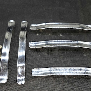 May include: A set of five polished chrome cabinet pulls with a curved, elongated design. Two pulls are positioned vertically on the left, while three are placed horizontally on the right. A small pile of metal mounting screws is included.