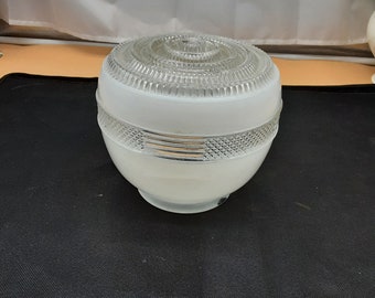May include: A white glass light fixture with a frosted finish and a clear, textured top. The fixture has a round shape and a decorative design.