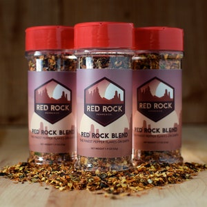 May include: Three glass jars with red lids filled with red pepper flakes. The jars are labeled "Red Rock Pepper Co." and "Red Rock Blend The Finest Pepper Flakes on Earth" with a net weight of 1.9 oz (53g).