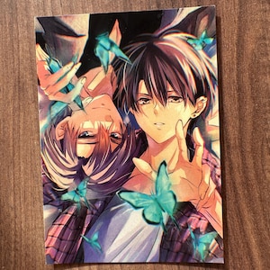Puede incluir: Impresión de estilo anime con dos figuras masculinas de cabello oscuro, rodeadas de mariposas turquesas. Una figura lleva una camisa a cuadros, la otra una camisa blanca. La obra de arte tiene una estética suave y colorida.