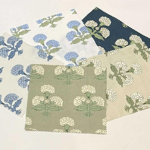 May include: A collection of fabric swatches with floral patterns. The swatches feature blue and white, and green and white floral designs. The fabric has a textured appearance and is arranged on a white surface.