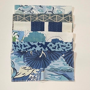 May include: A stack of six fabric swatches in various shades of blue with floral and geometric patterns. The swatches are arranged in a vertical stack, with the top swatch being a light blue floral pattern and the bottom swatch being a dark blue floral pattern.