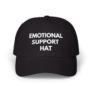 Könnte beinhalten: Schwarze Baseballkappe mit dem weißen Text "EMOTIONAL SUPPORT HAT". Die Kappe hat einen gebogenen Schirm und eine strukturierte Krone. Ein klassischer Hutstil, geeignet für Freizeitkleidung.