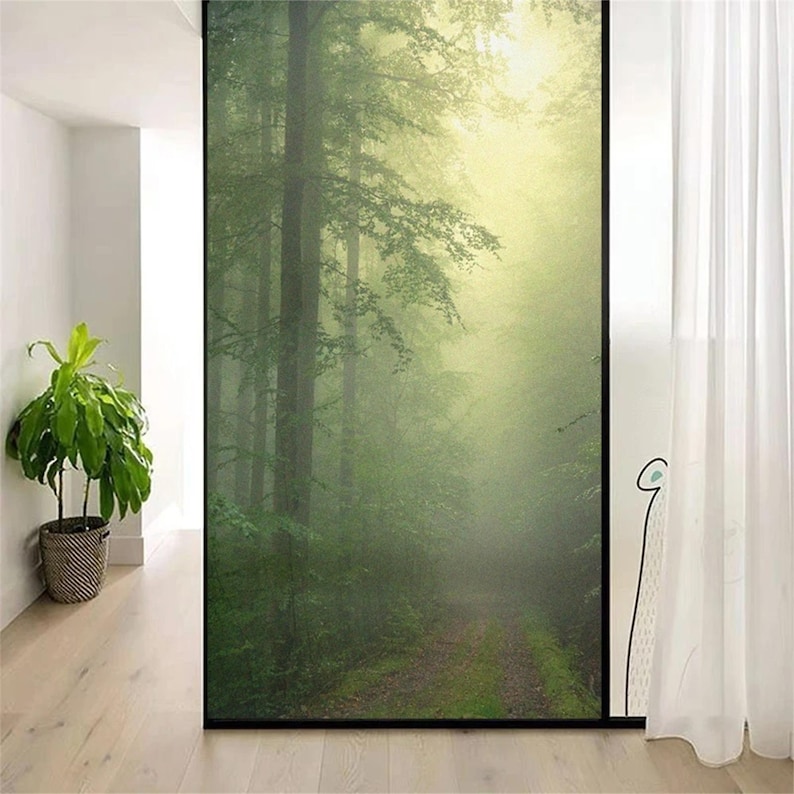 May include: A window film with a misty forest scene. The image shows a path leading into a dense forest with tall trees and a soft, green glow.