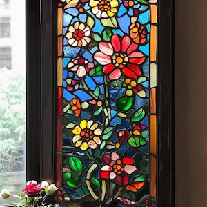 以下が含まれることがあります： 赤、ピンク、黄色、緑の花が咲く花柄のステンドグラスの窓。窓は黒い木枠で囲まれています。