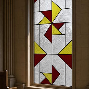 Op de afbeelding: Een rechthoekig glas-in-loodraam met een geometrisch patroon van heldere, getextureerde glaspanelen afgewisseld met massieve driehoekige vormen in felgeel en dieprood, samengevoegd door dunne zwarte loodlijnen in een rasterontwerp.