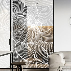 Puede incluir: Una puerta de vidrio con un diseño floral blanco. El diseño presenta una flor grande y estilizada con líneas intrincadas y fluidas. La puerta está enmarcada en negro, con un fondo de tonos neutros.