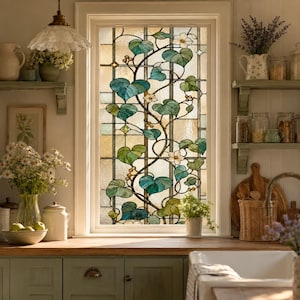 Op de afbeelding: Een rechthoekig raam met een glas-in-loodpaneel met een klimplantmotief. Het ontwerp toont blauwgroene en groene hartvormige bladeren, kleine witte bloemen en amberkleurige bessen tegen een raster van helder, getextureerd glas.