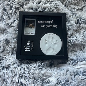May include: Black framed memorial with a white paw print, a photo of a dog, and the text "in memory of our guard dog Max 2016-2022 10/18/2018"