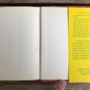 May include: A yellow and red book with the title "Quick and Easy Recipes for Two" by Louella G. Shouer, associate food editor of the Ladies Home Journal. The book is published by Bramhall House, distributed by Crown Publishers, Inc. 417 Park Avenue South, New York, NY 10016.