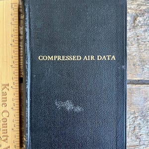 Könnte beinhalten: Ein schwarzes, ledergebundenes Buch mit goldener Aufschrift "COMPRESSED AIR DATA".