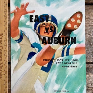 Könnte beinhalten: Ein Vintage-Programm für ein Footballspiel zwischen East und Auburn. Das Programm zeigt eine farbenfrohe Illustration eines Footballspielers, der einen Pass fängt. Das Spiel fand am Freitag, den 27. Oktober 1961, im Roy E. Davis Field in Aurora, Illinois, statt. Das Programm kostete 10 Cent.
