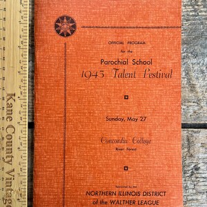 以下が含まれることがあります： 1945年のタレントフェスティバルのオレンジ色のプログラムカバー。テキストとサンバーストのデザインが特徴です。プログラムはConcordia Collegeで開催されたParochial Schoolのものです。木製の定規が隣にあります。